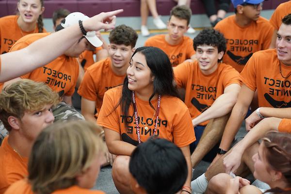 Students in matching shirts sitting on the ground wearing AQ lanyards